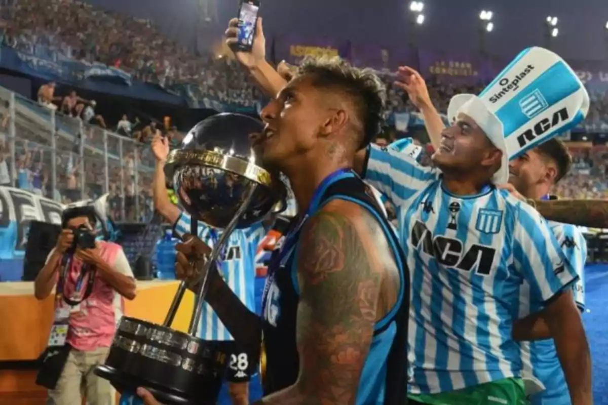 Jugadores de fútbol celebran con un trofeo en un estadio lleno de aficionados.