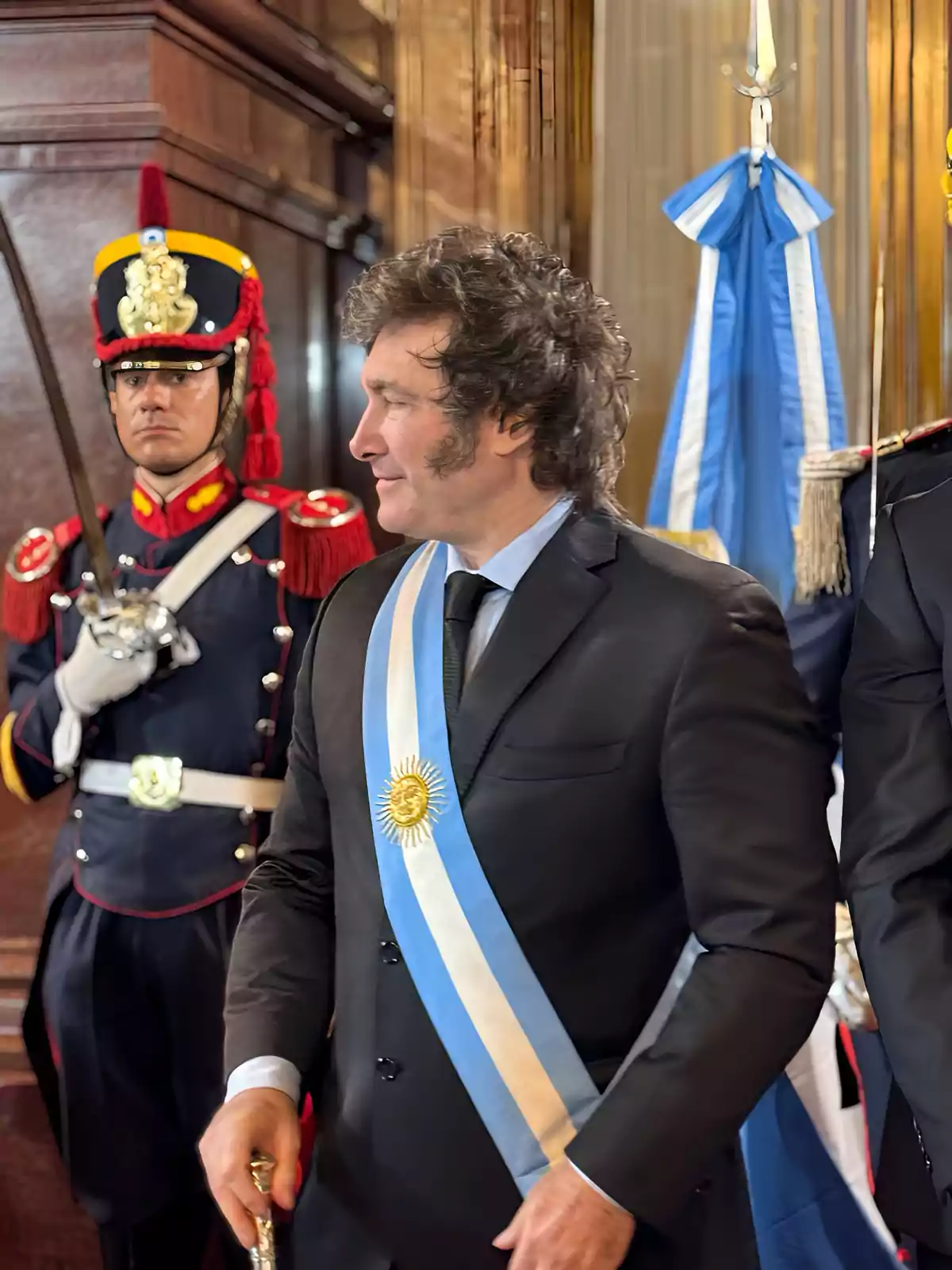 Hombre con banda presidencial argentina y traje oscuro acompañado por un guardia con uniforme ceremonial y bandera argentina de fondo Hombre con banda presidencial argentina y traje oscuro acompañado por un guardia con uniforme ceremonial y bandera argentina de fondo