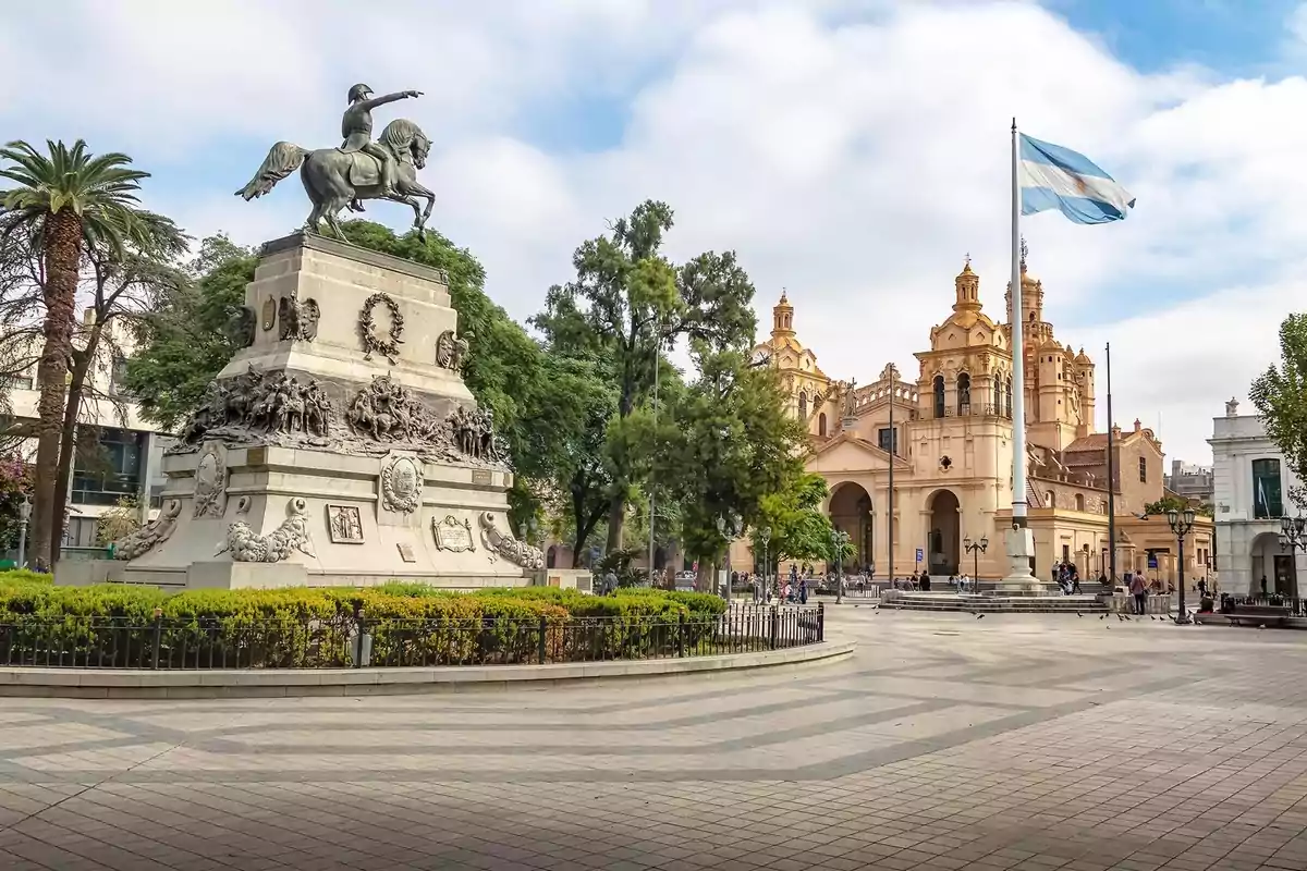 Plaza principal de una ciudad con un monumento ecuestre, una catedral al fondo y una bandera argentina ondeando