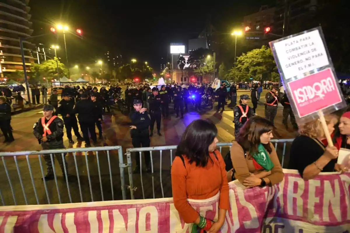Women protesting in front of a group of police officers on a street lit up at night, with signs and barricades between them Women protesting in front of a group of police officers on a street lit up at night, with signs and barricades between them