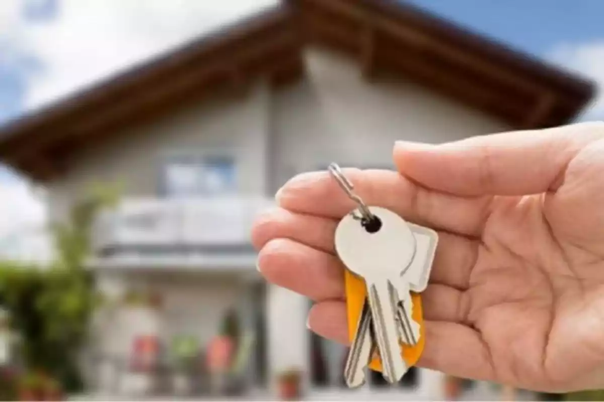 A hand holding a keychain with several keys in front of a blurred house. A hand holding a keychain with several keys in front of a blurred house.