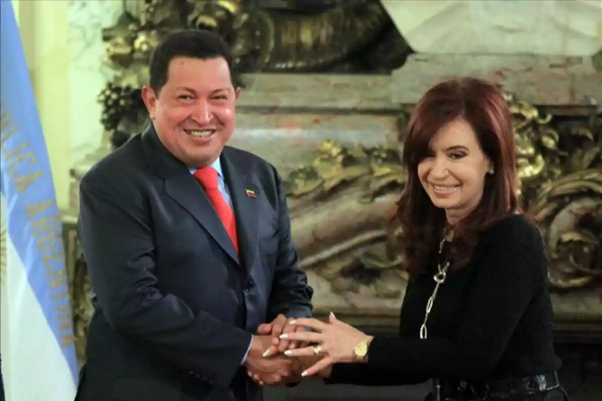 Dos personas sonrientes se dan la mano en un entorno formal con una bandera de Argentina al fondo.