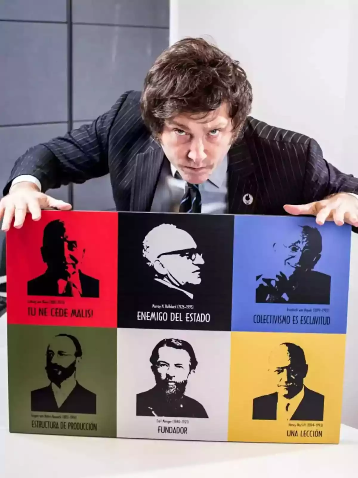 Hombre de cabello castaño y traje oscuro inclinado sobre un cartel colorido con retratos y frases de economistas famosos Hombre de cabello castaño y traje oscuro inclinado sobre un cartel colorido con retratos y frases de economistas famosos