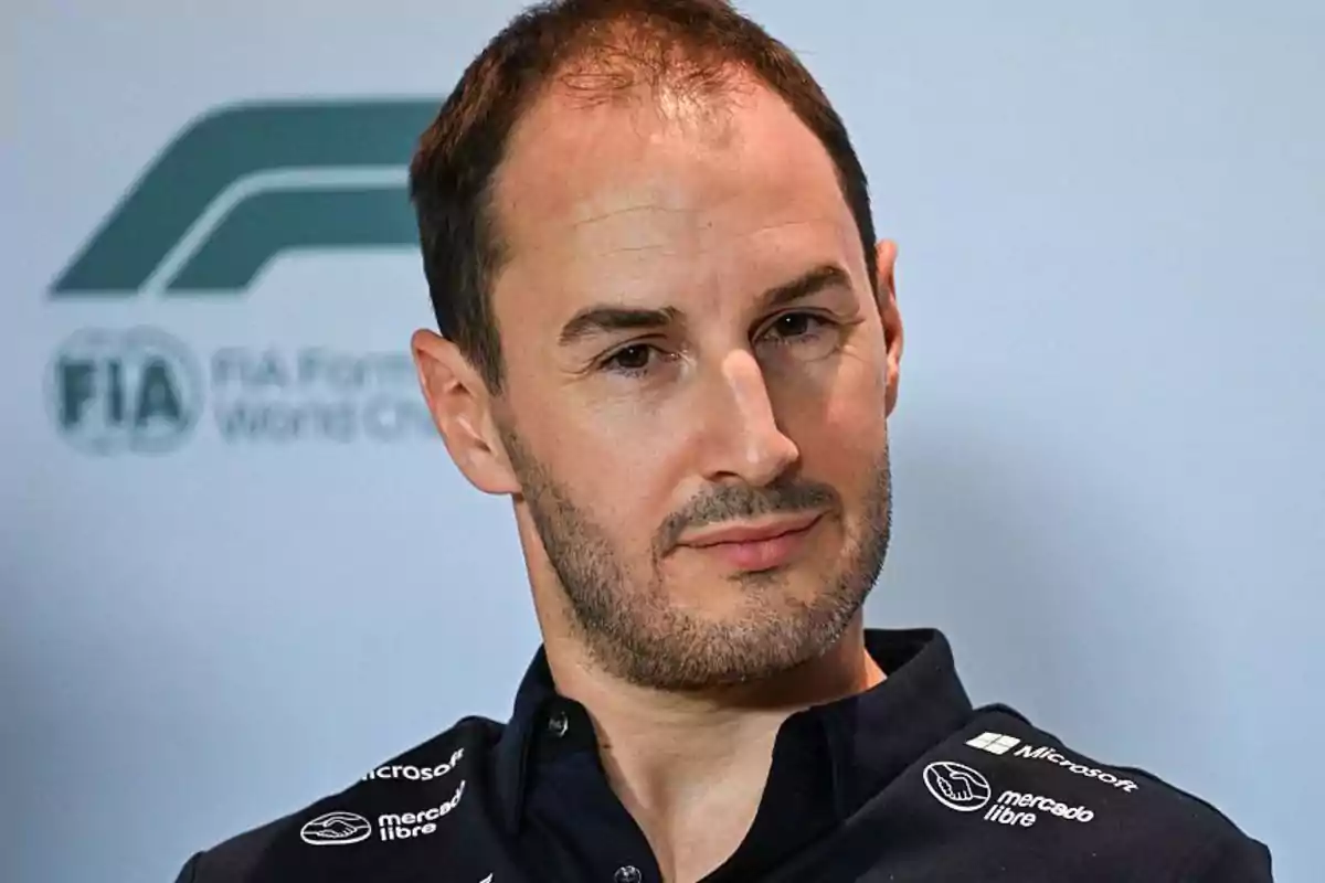 Un hombre con barba y cabello corto lleva una camisa oscura con logotipos, posando frente a un fondo con el logotipo de la FIA. Un hombre con barba y cabello corto lleva una camisa oscura con logotipos, posando frente a un fondo con el logotipo de la FIA.