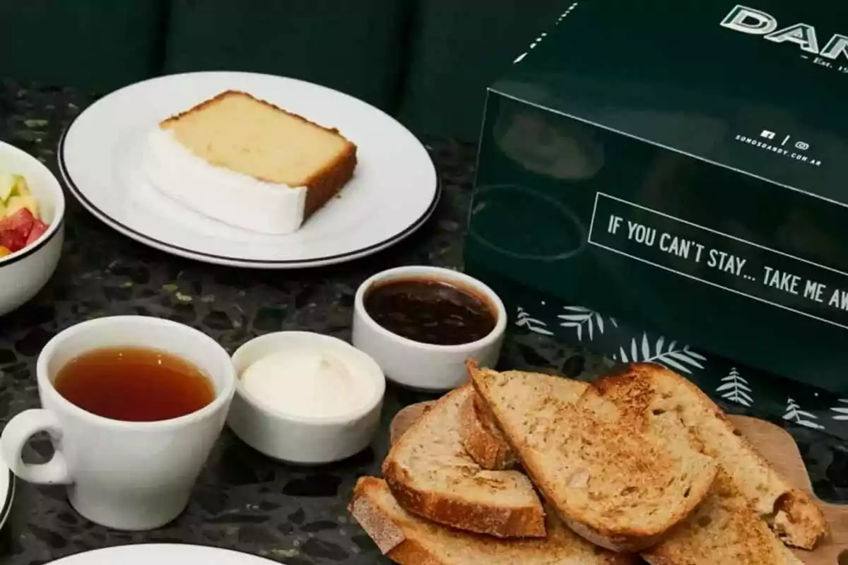 Breakfast with slices of toasted bread, jam, cream, tea, cake, and a green box on a table Breakfast with slices of toasted bread, jam, cream, tea, cake, and a green box on a table