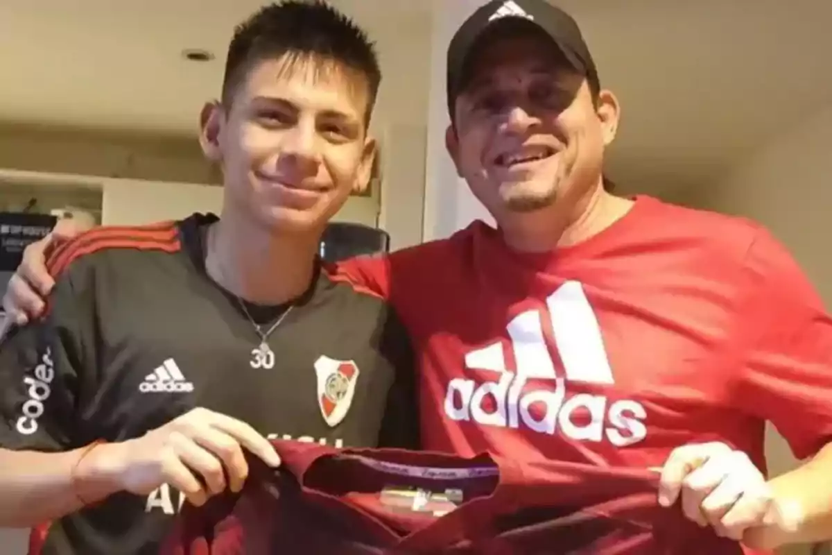Dos personas sonríen mientras sostienen una camiseta de fútbol en una habitación iluminada. Dos personas sonríen mientras sostienen una camiseta de fútbol en una habitación iluminada.