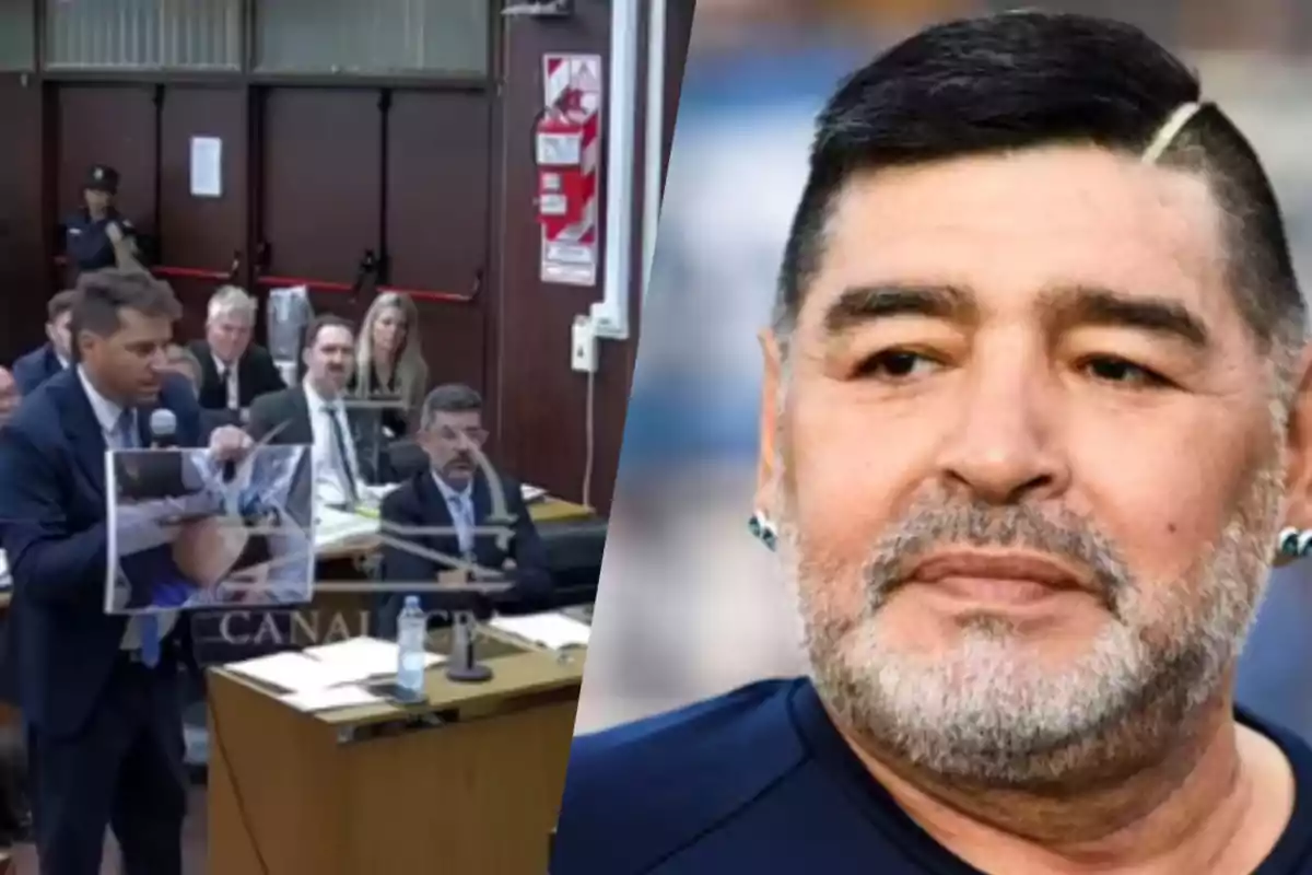 A man in a courtroom holds a picture while speaking, with several people seated behind him, next to a portrait of a man with a beard and dark hair.