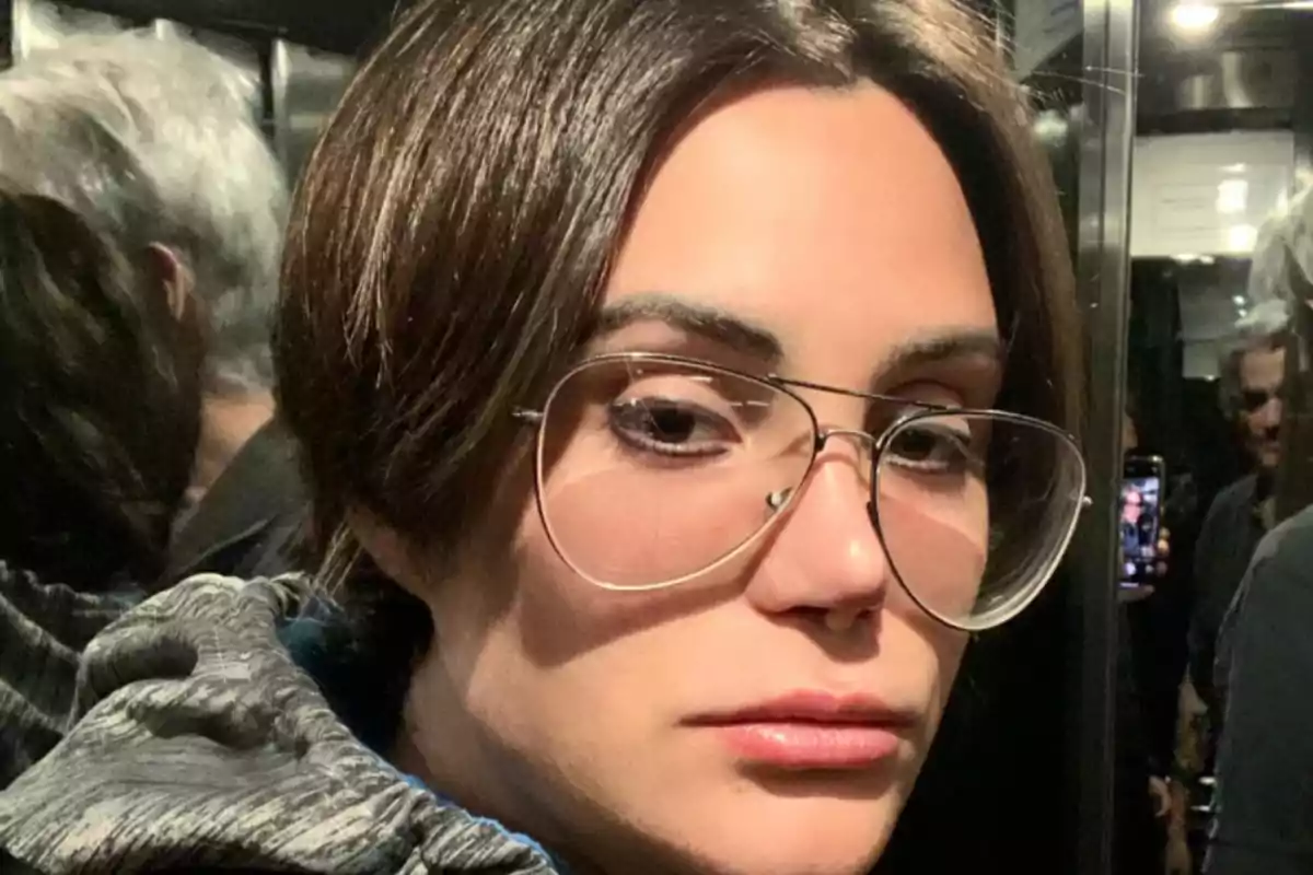 Una persona con gafas grandes y cabello corto está en un lugar con espejos. Una persona con gafas grandes y cabello corto está en un lugar con espejos.