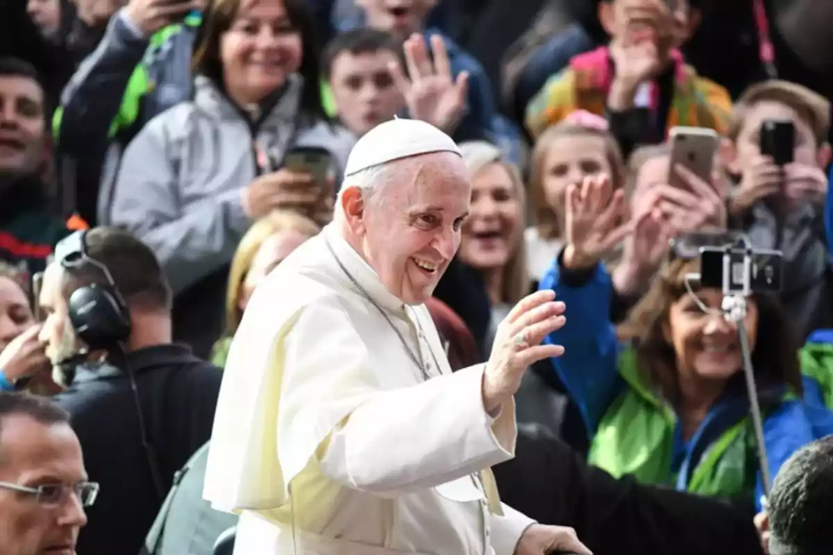 A religious figure greets a crowd of people who surround him and take pictures. A religious figure greets a crowd of people who surround him and take pictures.