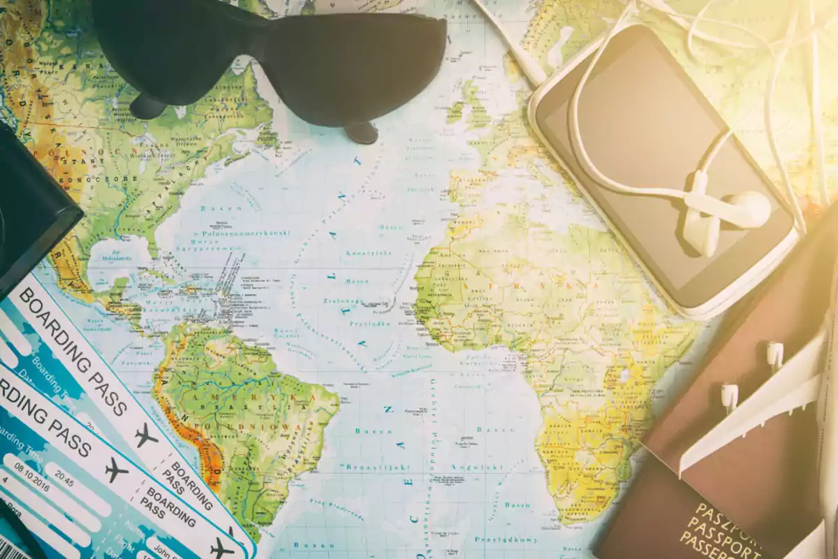 Mapa del mundo con gafas de sol, boletos de embarque, un teléfono con auriculares y un pasaporte. Mapa del mundo con gafas de sol, boletos de embarque, un teléfono con auriculares y un pasaporte.