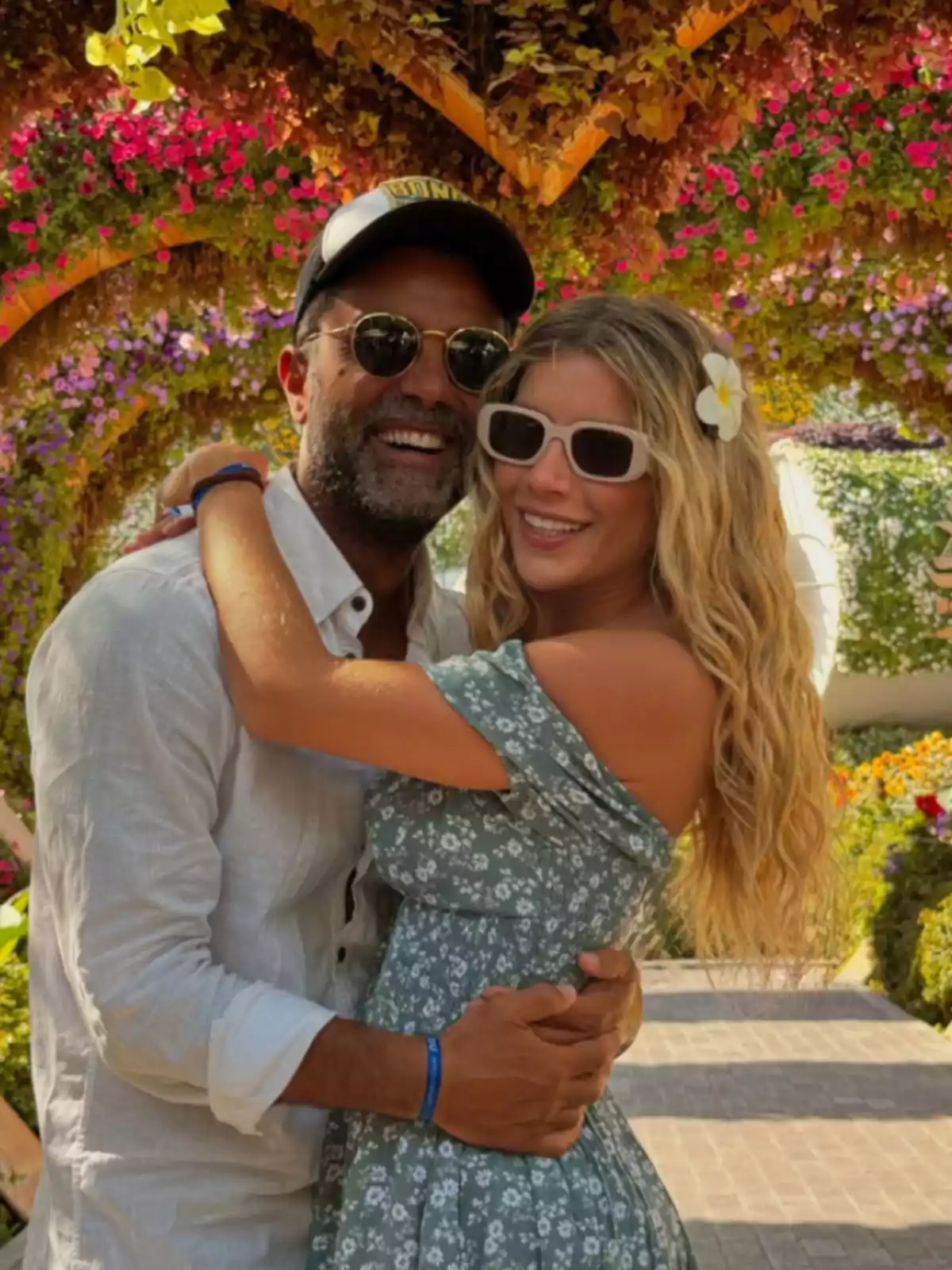 Una pareja sonriente se abraza bajo un arco floral colorido en un jardín. Una pareja sonriente se abraza bajo un arco floral colorido en un jardín.