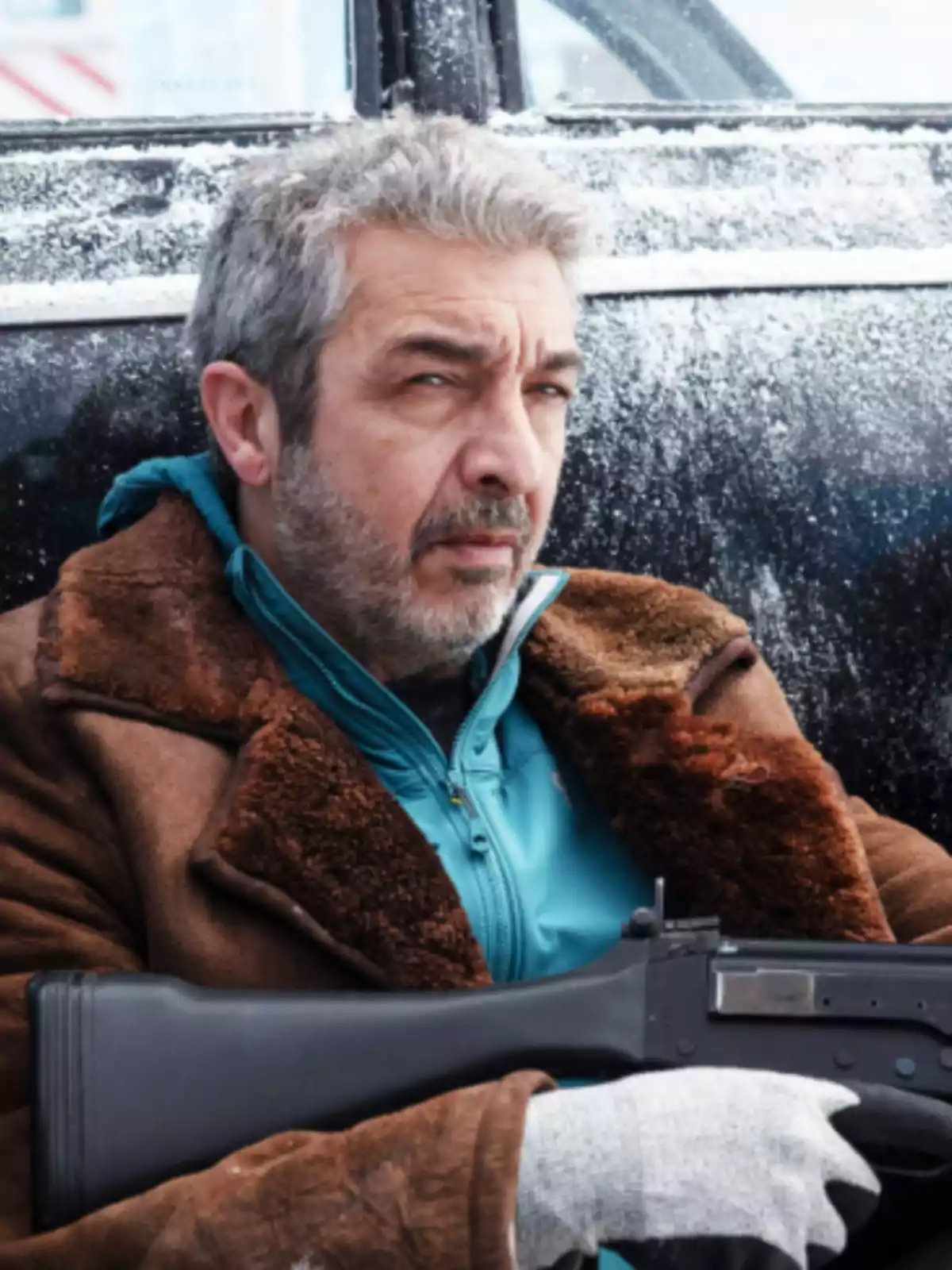 Hombre con abrigo marrón y guantes grises sosteniendo un arma frente a un vehículo cubierto de nieve. Hombre con abrigo marrón y guantes grises sosteniendo un arma frente a un vehículo cubierto de nieve.