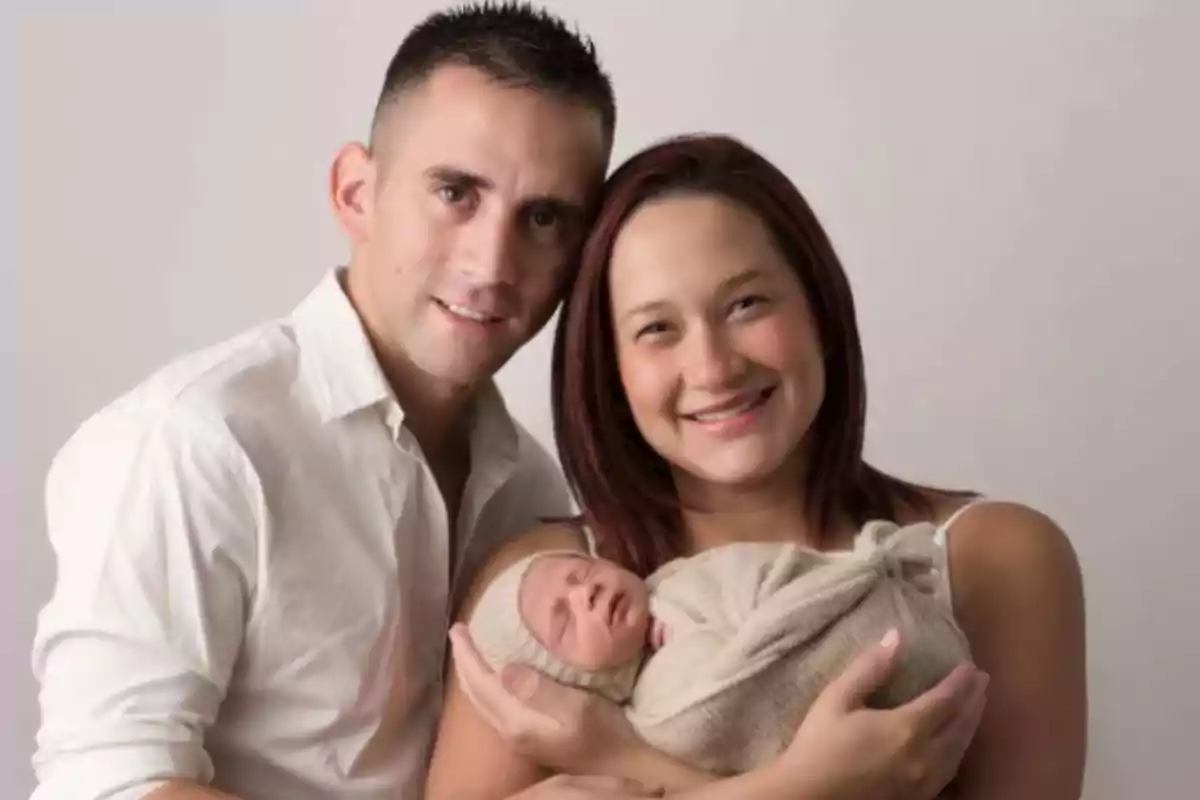 Una pareja sonriente sostiene a un bebé envuelto en una manta. Una pareja sonriente sostiene a un bebé envuelto en una manta.