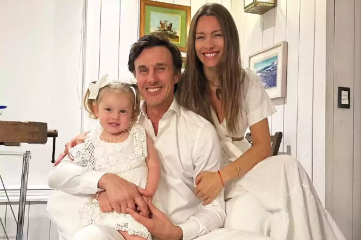 Una familia sonriente posando en una sala con paredes blancas y cuadros en la pared.