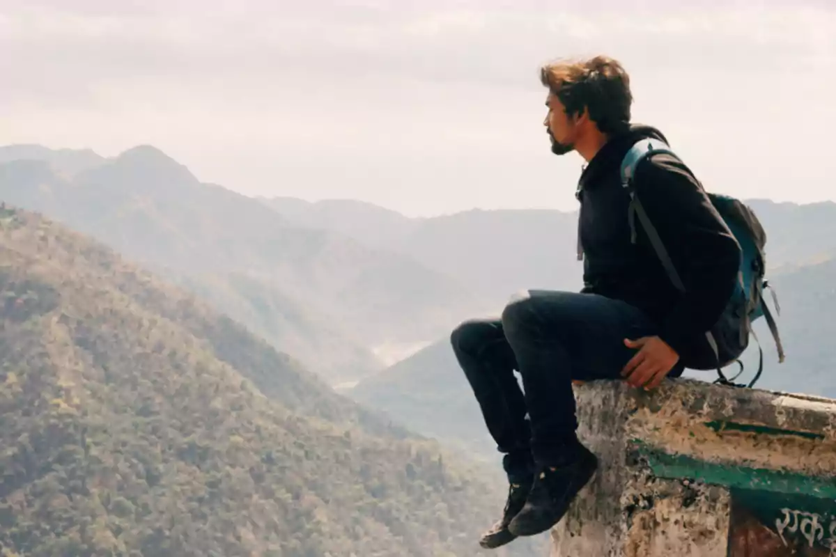 Un hombre con mochila sentado en un muro contemplando un paisaje montañoso. Un hombre con mochila sentado en un muro contemplando un paisaje montañoso.