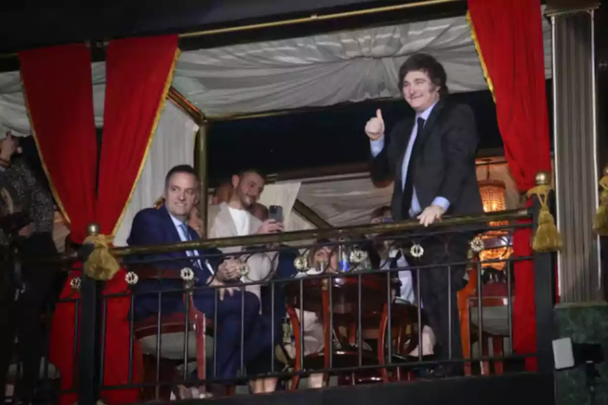 A group of people on a balcony decorated with red curtains, one of them giving a thumbs-up as a sign of approval. A group of people on a balcony decorated with red curtains, one of them giving a thumbs-up as a sign of approval.