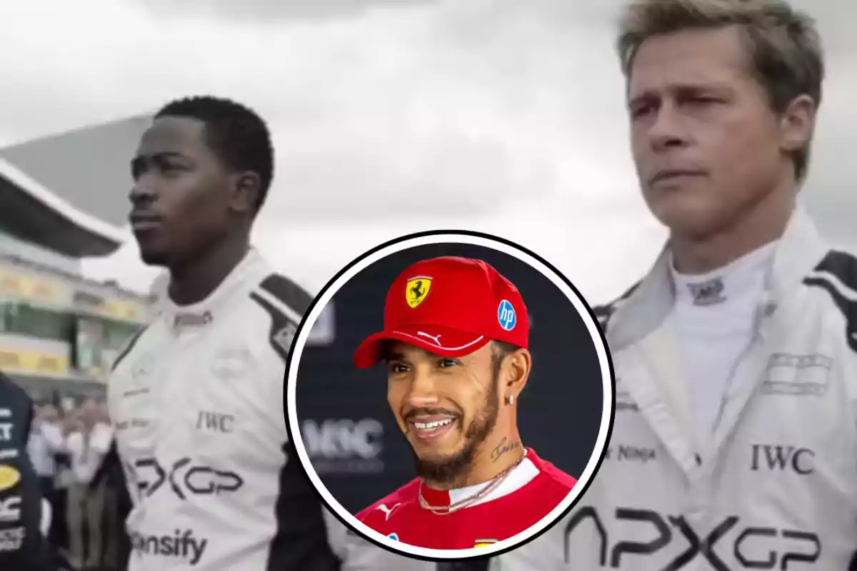 Two people in racing suits are standing on a track, while in a box a man with a red cap is smiling.