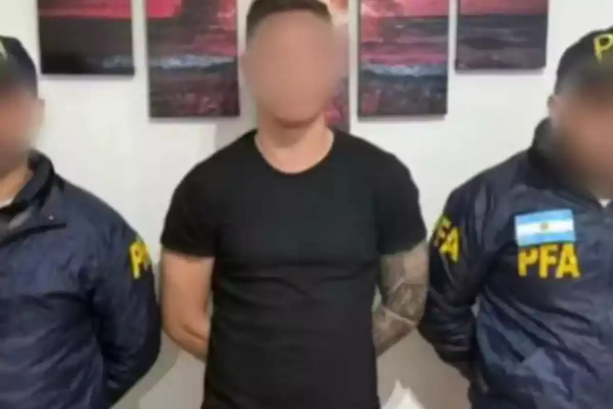 Tres personas de pie, dos con chaquetas de la PFA y una en el centro con camiseta negra, con los rostros difuminados.