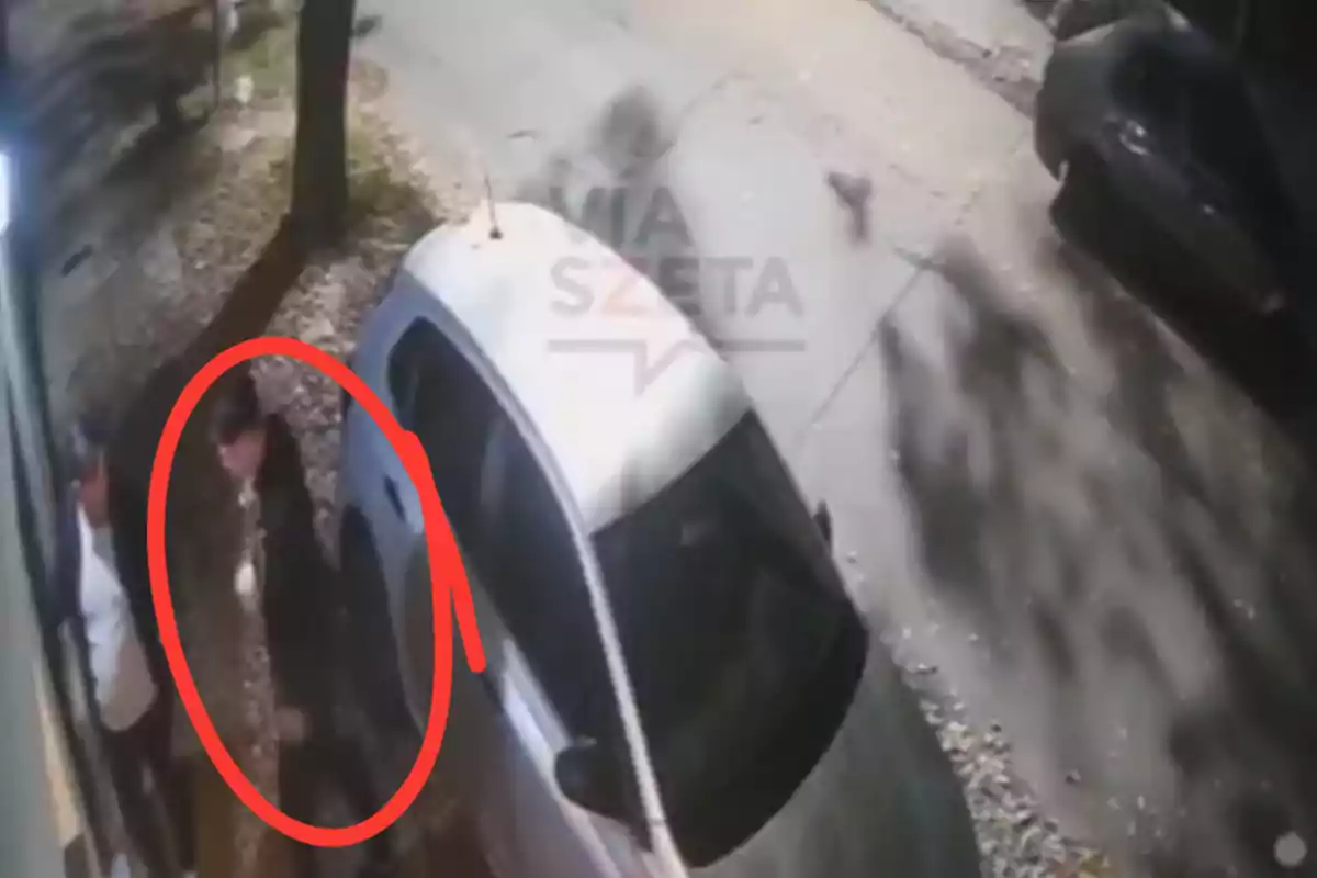 Two people are standing next to a car parked on a street, one of them is surrounded by a red circle. Two people are standing next to a car parked on a street, one of them is surrounded by a red circle.