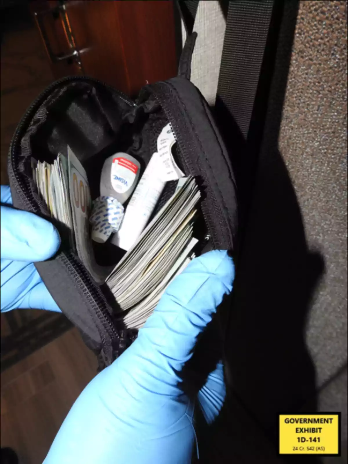 A hand in blue gloves holds an open black bag containing bundles of bills and some small items. A hand in blue gloves holds an open black bag containing bundles of bills and some small items.