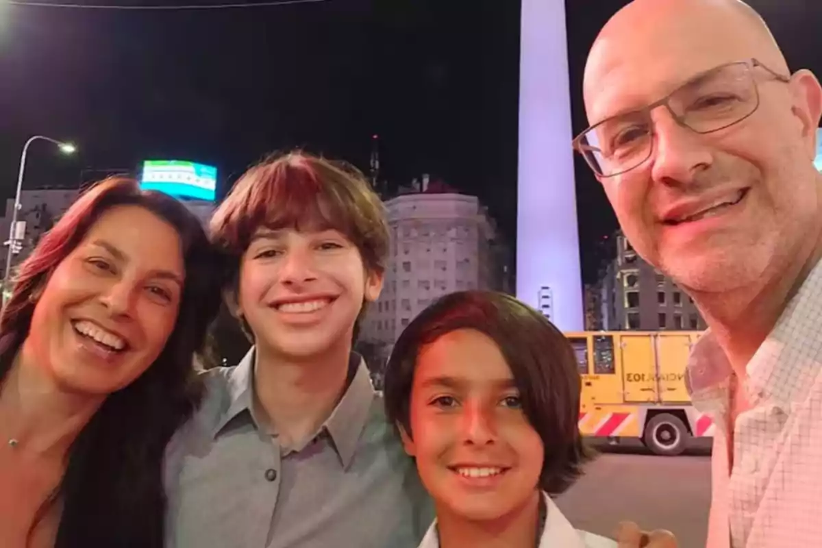Una familia sonriente posando frente al Obelisco de Buenos Aires por la noche.