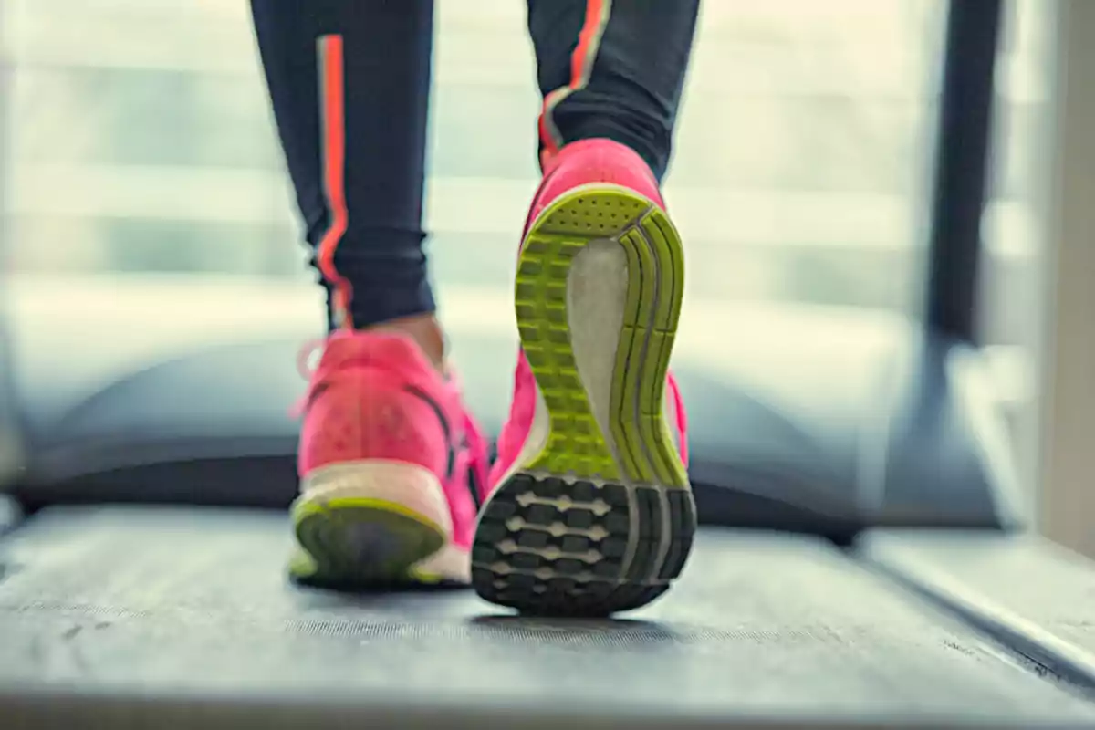 Persona corriendo en una caminadora con zapatillas deportivas rosas. Persona corriendo en una caminadora con zapatillas deportivas rosas.