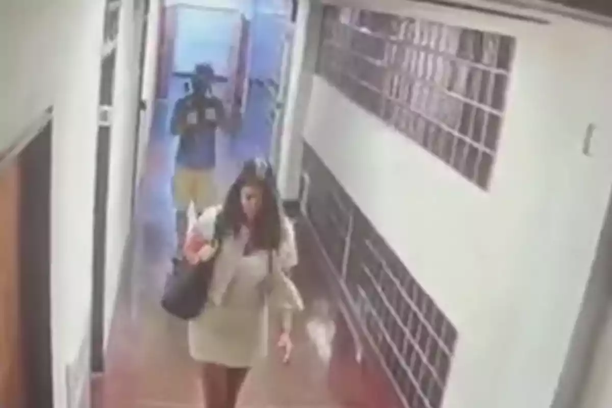 A woman walks down a hallway while a man follows her at a distance. A woman walks down a hallway while a man follows her at a distance.