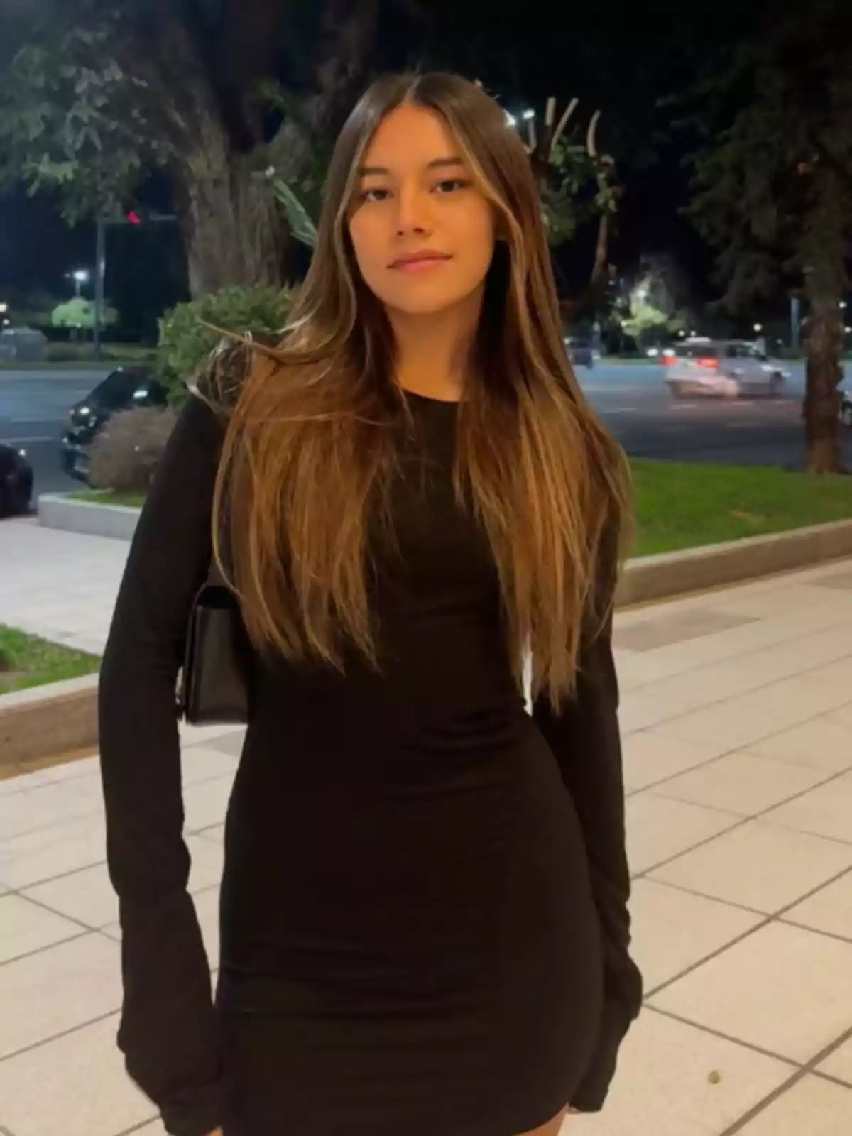 Young woman in a black dress posing outdoors on a sidewalk at night Young woman in a black dress posing outdoors on a sidewalk at night