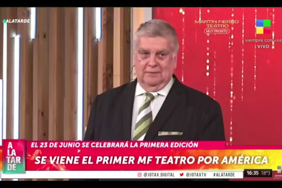 Older man with gray hair wearing a dark suit and a green striped tie on a television set with a red background and a sign announcing the first edition of the Martín Fierro Theater Awards by América. Older man with gray hair wearing a dark suit and a green striped tie on a television set with a red background and a sign announcing the first edition of the Martín Fierro Theater Awards by América.