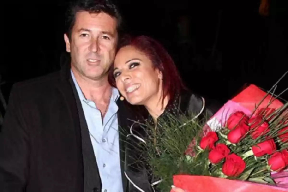 Pareja posando sonriente mientras la mujer sostiene un ramo de rosas rojas Pareja posando sonriente mientras la mujer sostiene un ramo de rosas rojas