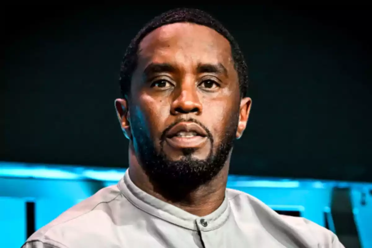 Short-bearded, short-haired man with a serious expression wearing a light gray jersey against a dark background