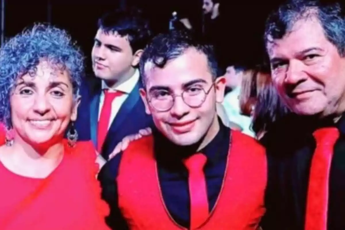 Three people smile at the camera at a formal event, all dressed in elegant red and black attire, with more attendees visible in the background. Three people smile at the camera at a formal event, all dressed in elegant red and black attire, with more attendees visible in the background.