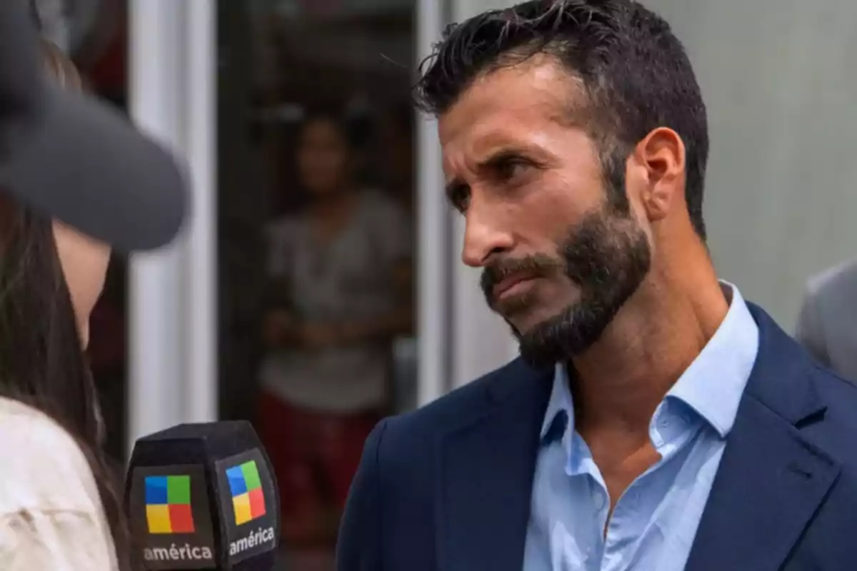 Bearded man in a blue jacket being interviewed by a reporter with an América microphone