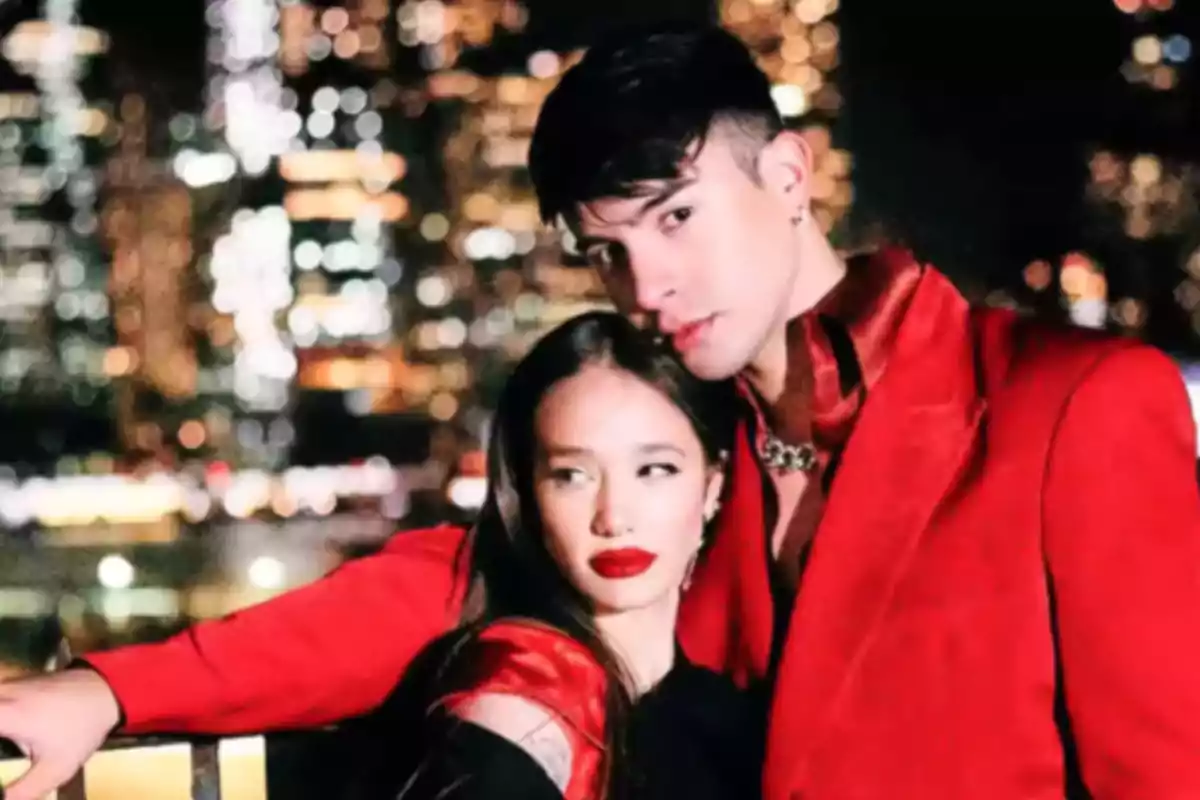 Young couple posing at night in elegant red-toned outfits with a brightly lit city background