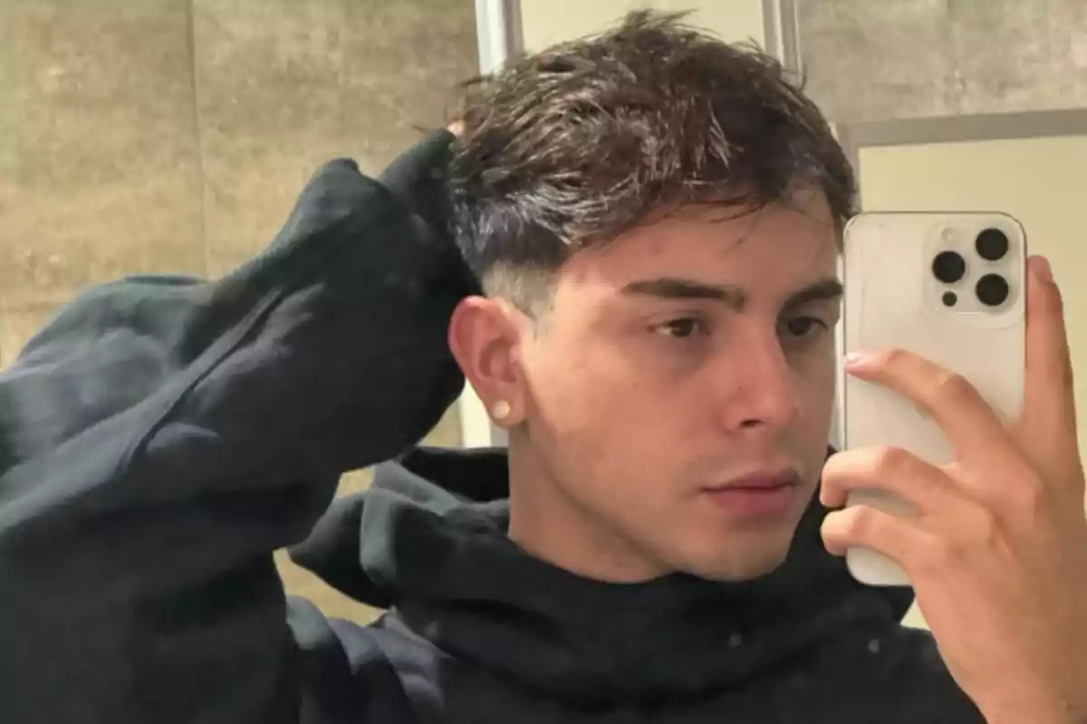 Young man in a black hoodie taking a selfie in front of the mirror with a white cell phone