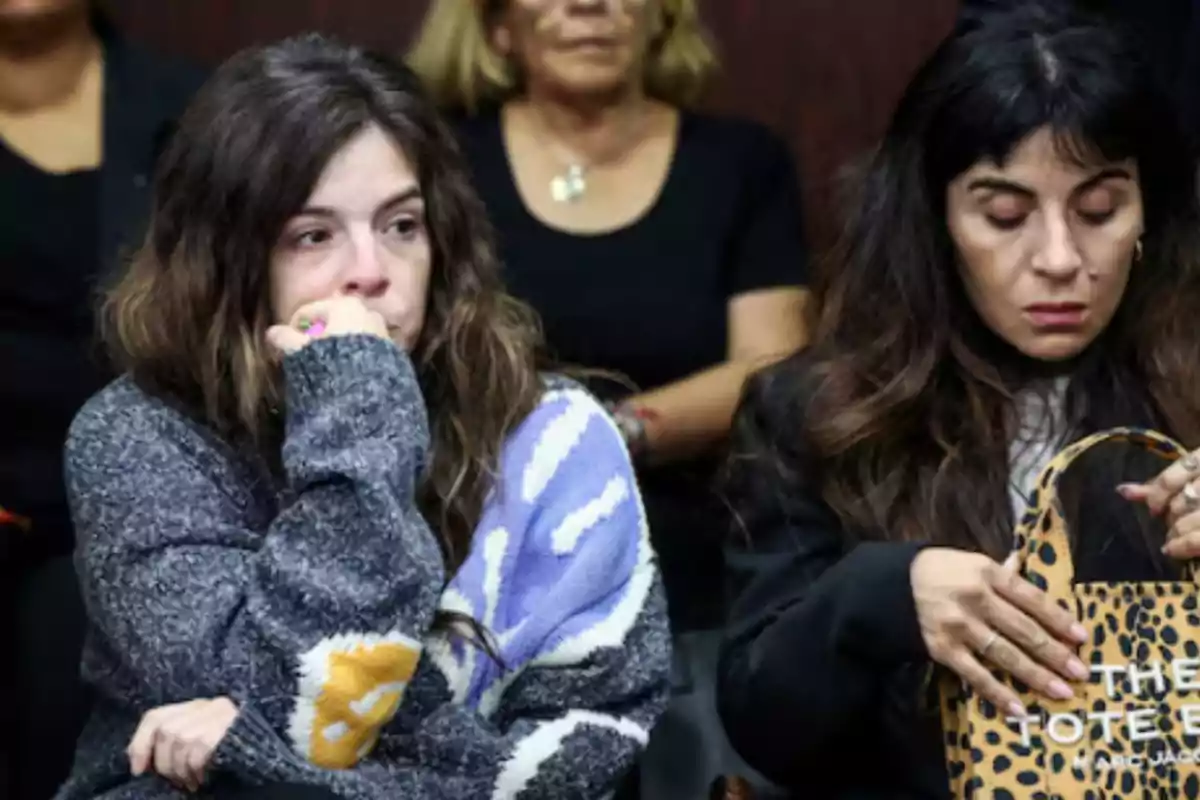 Two women are sitting in what appears to be a living room; one of them looks worried while the other is checking the inside of an animal print purse. Two women are sitting in what appears to be a living room; one of them looks worried while the other is checking the inside of an animal print purse.