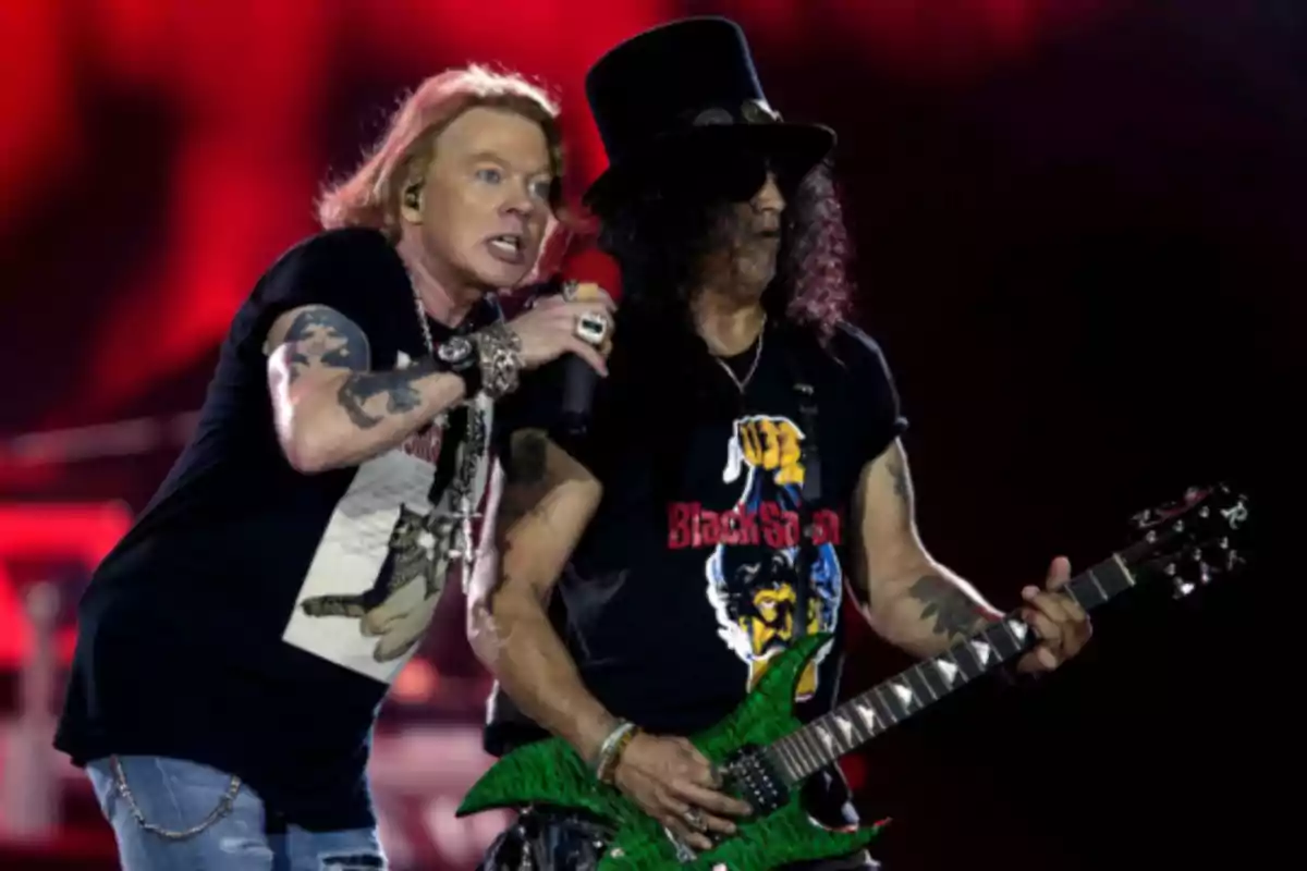 Two rock musicians performing on stage, one singing with a microphone and the other playing a green electric guitar, with a red-lit background