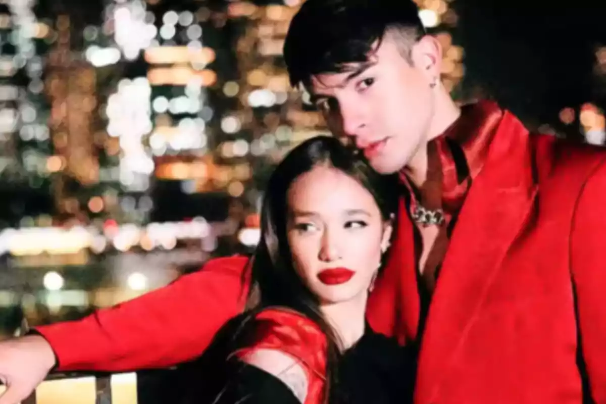 Una pareja joven posa abrazada con ropa elegante de color rojo y negro frente a un fondo de luces de ciudad desenfocadas por la noche Una pareja joven posa abrazada con ropa elegante de color rojo y negro frente a un fondo de luces de ciudad desenfocadas por la noche