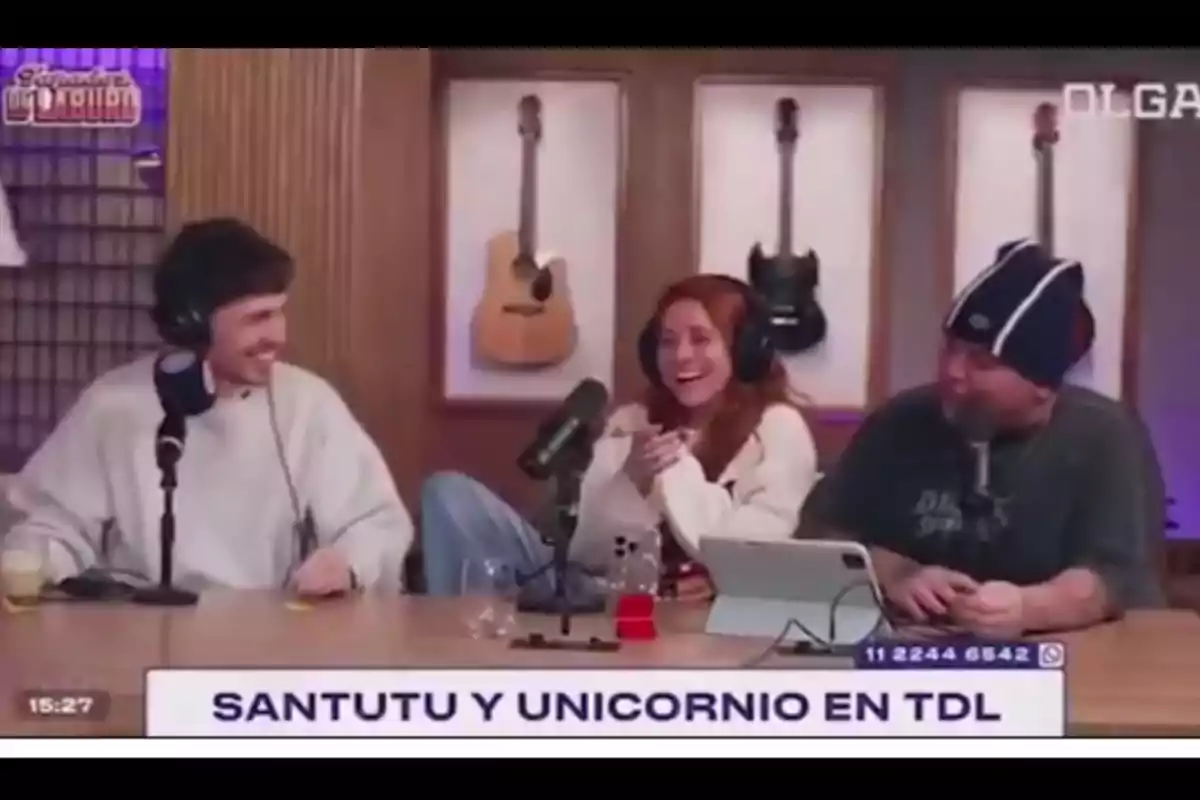 Three people sitting at a radio or podcast studio table, laughing and talking in front of microphones, with guitars hanging on the wall in the background and a sign on the screen that says SANTUTU AND UNICORN IN TDL. Three people sitting at a radio or podcast studio table, laughing and talking in front of microphones, with guitars hanging on the wall in the background and a sign on the screen that says SANTUTU AND UNICORN IN TDL.