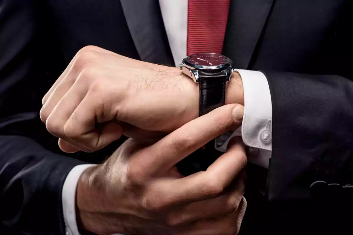 Hombre de negocios ajustando su reloj de pulsera mientras viste traje y corbata roja Hombre de negocios ajustando su reloj de pulsera mientras viste traje y corbata roja