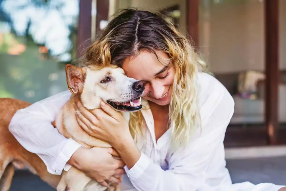 Mujer abrazando y sonriendo junto a un perro en un ambiente hogareño Mujer abrazando y sonriendo junto a un perro en un ambiente hogareño