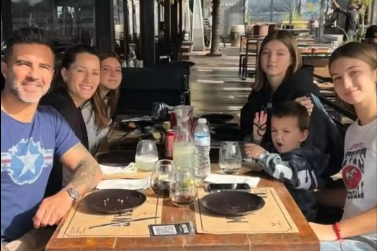 Una familia sentada alrededor de una mesa en un restaurante al aire libre disfrutando de una comida juntos Una familia sentada alrededor de una mesa en un restaurante al aire libre disfrutando de una comida juntos
