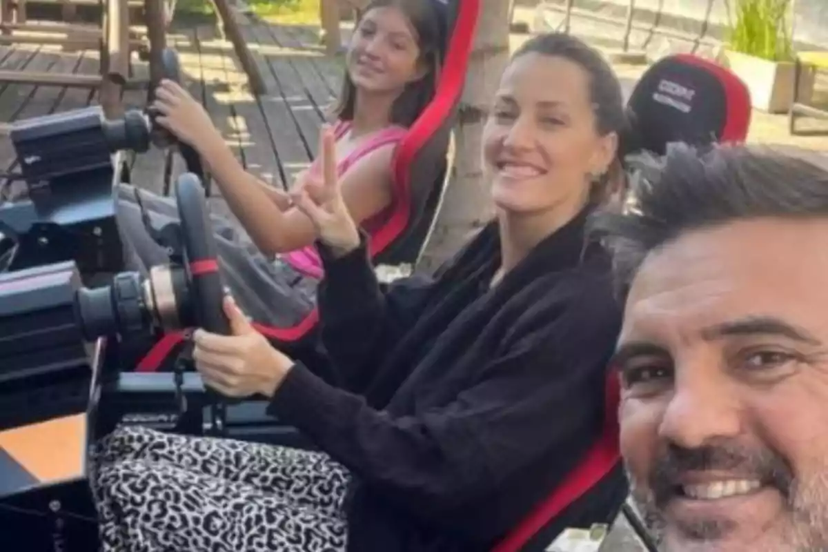 Tres personas sonríen mientras disfrutan de un simulador de manejo al aire libre Tres personas sonríen mientras disfrutan de un simulador de manejo al aire libre