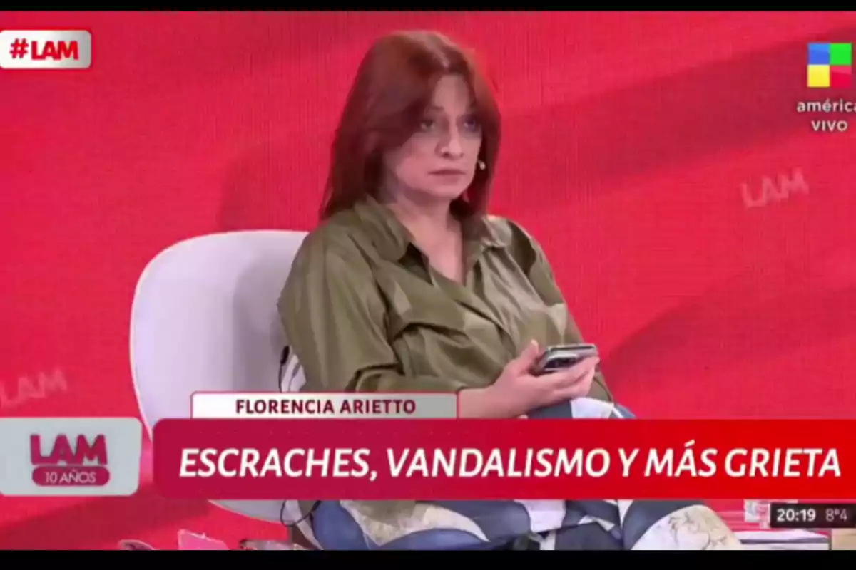 Mujer de cabello rojizo sentada en un programa de televisión con fondo rojo sosteniendo un celular y expresión seria, en la pantalla se lee el nombre Florencia Arietto y el texto escraches, vandalismo y más grieta Mujer de cabello rojizo sentada en un programa de televisión con fondo rojo sosteniendo un celular y expresión seria, en la pantalla se lee el nombre Florencia Arietto y el texto escraches, vandalismo y más grieta
