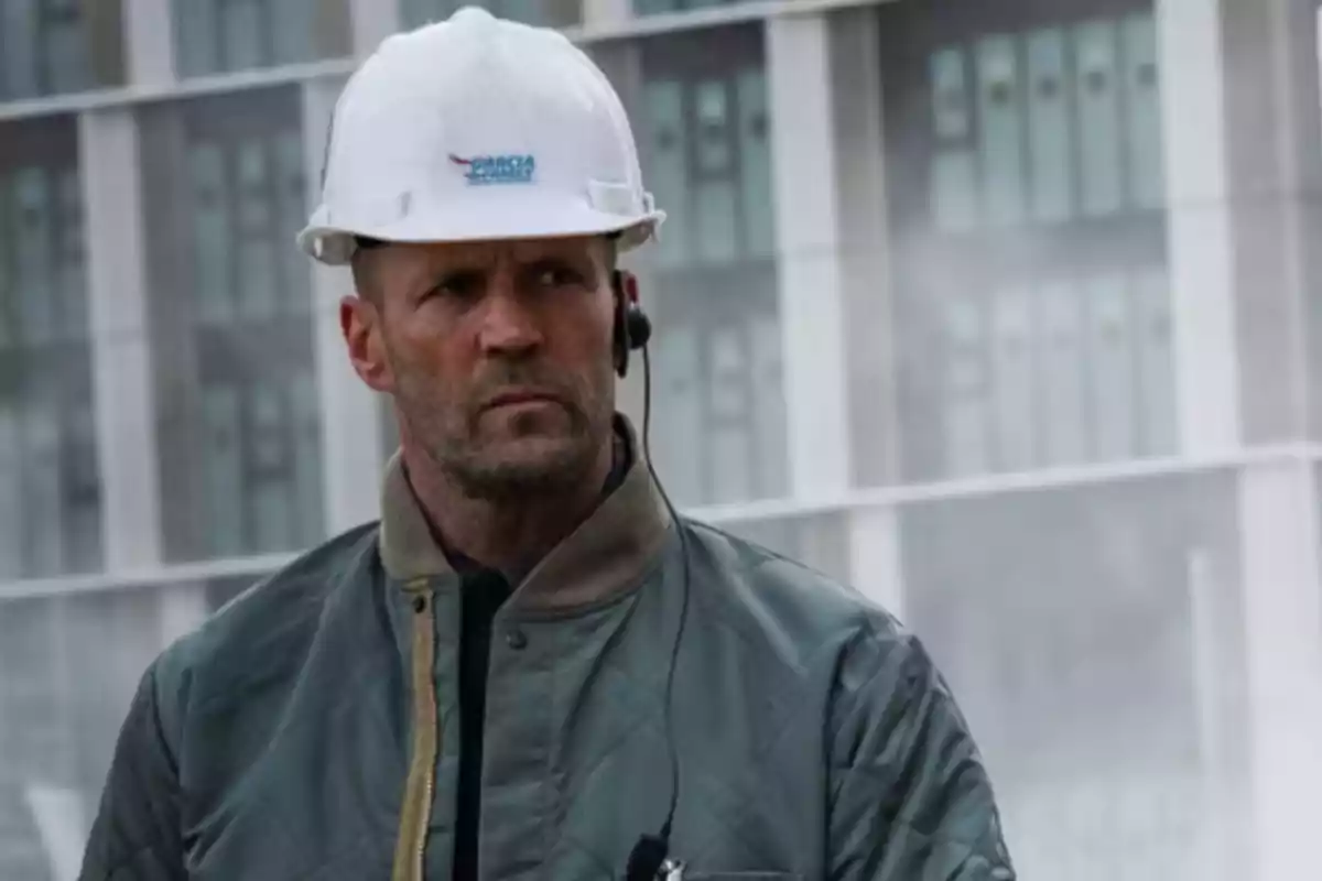 Hombre con casco de seguridad blanco y chaqueta verde frente a un edificio moderno