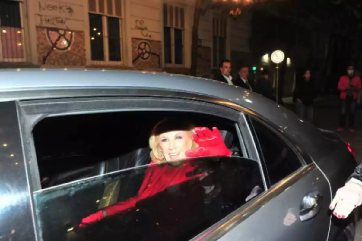 Blonde woman with red gloves waving from the window of a silver car at night Blonde woman with red gloves waving from the window of a silver car at night
