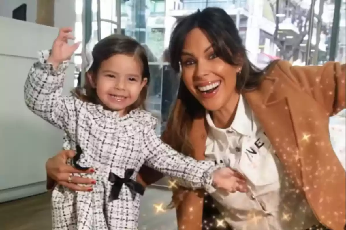 Una mujer y una niña sonríen y posan felices juntas en un ambiente interior con destellos brillantes alrededor.