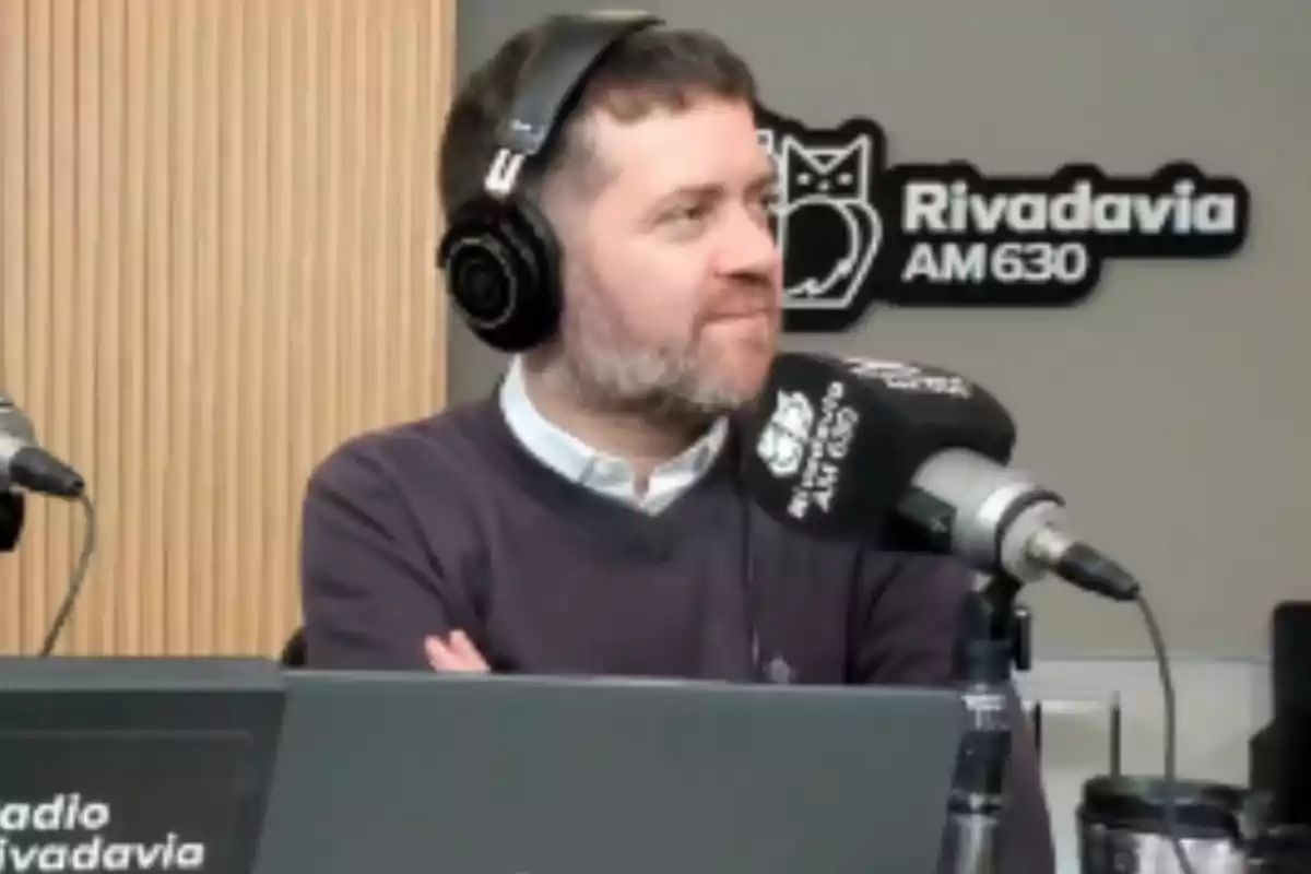 Man wearing headphones sitting in front of a microphone in a radio studio with the Radio Rivadavia AM 630 logo in the background Man wearing headphones sitting in front of a microphone in a radio studio with the Radio Rivadavia AM 630 logo in the background