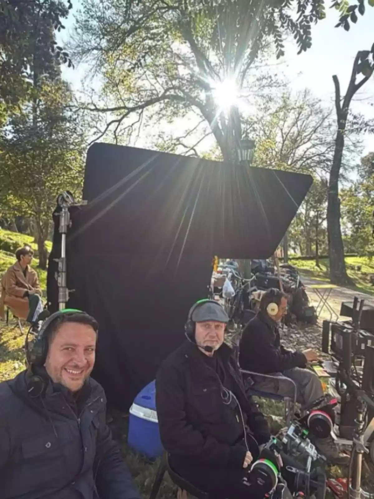 Several people with headphones and microphones sitting in front of recording equipment on an outdoor film set with trees and sunlight in the background Several people with headphones and microphones sitting in front of recording equipment on an outdoor film set with trees and sunlight in the background