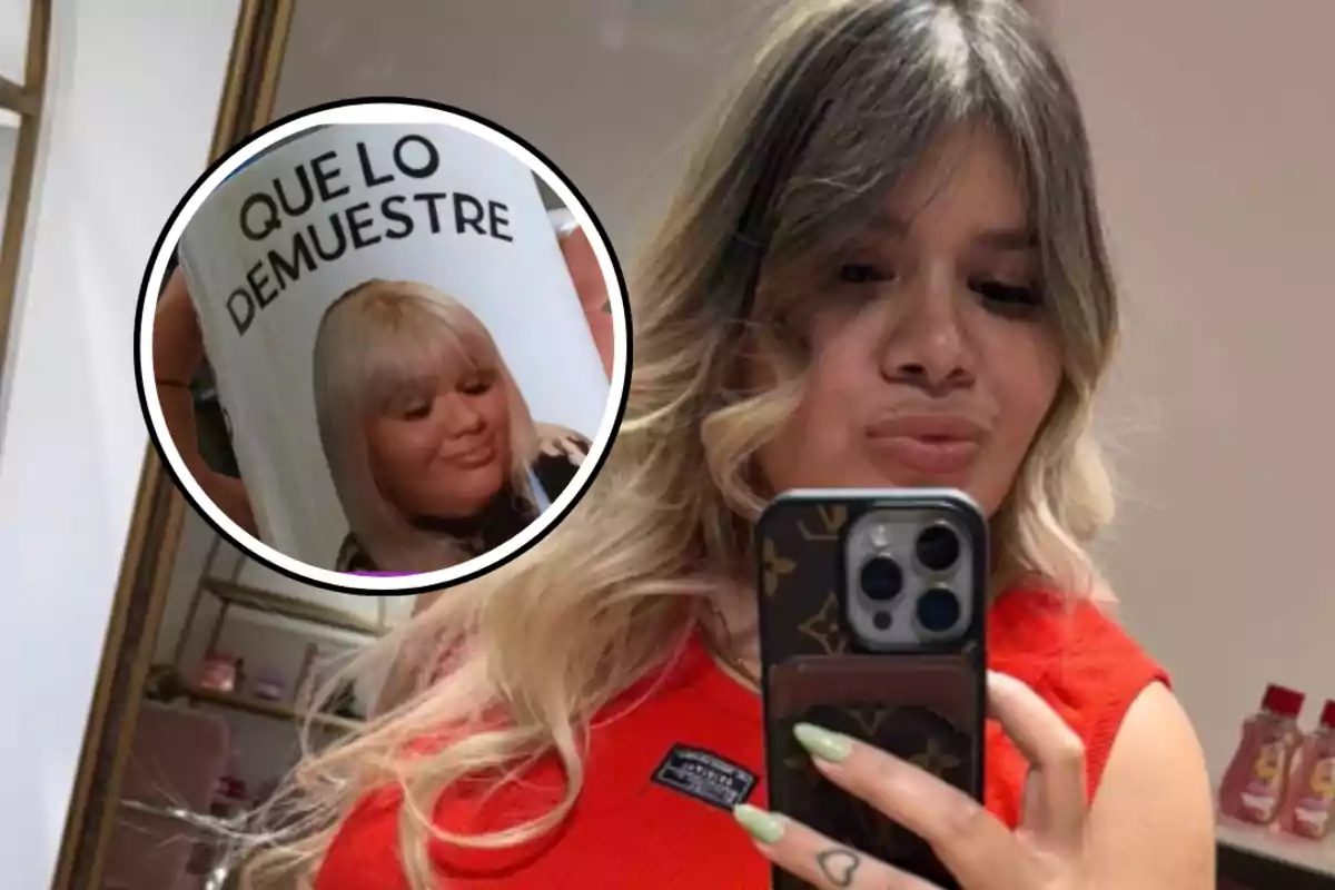 Una persona con cabello rubio y largo se toma una selfie frente a un espejo, sosteniendo un teléfono móvil; en la esquina de la imagen hay un recuadro que muestra una taza con la frase "QUE LO DEMUESTRE" y la imagen de una mujer rubia.